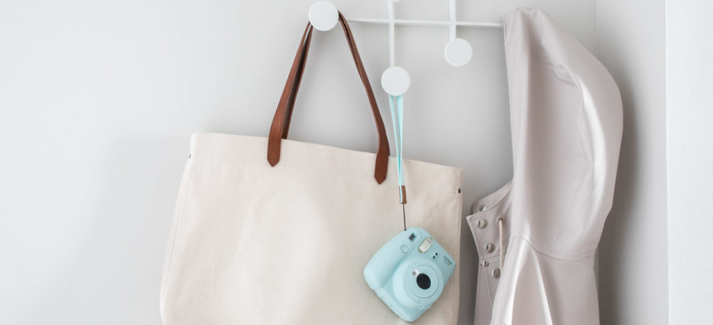 Detail of Wall Hooks on White Wall with Hanging Beige Tote Bag, Light Blue Camera and Light Gray Jacket