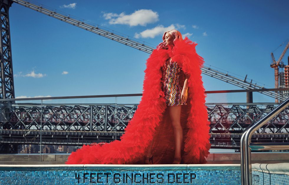 Iggy Azalea in dress and extravagant, large, bold, red boa scarf at the edge of 420 Kent pool with bridge in the background